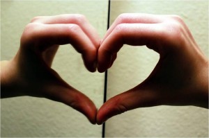 Two hands make a heart over an open book